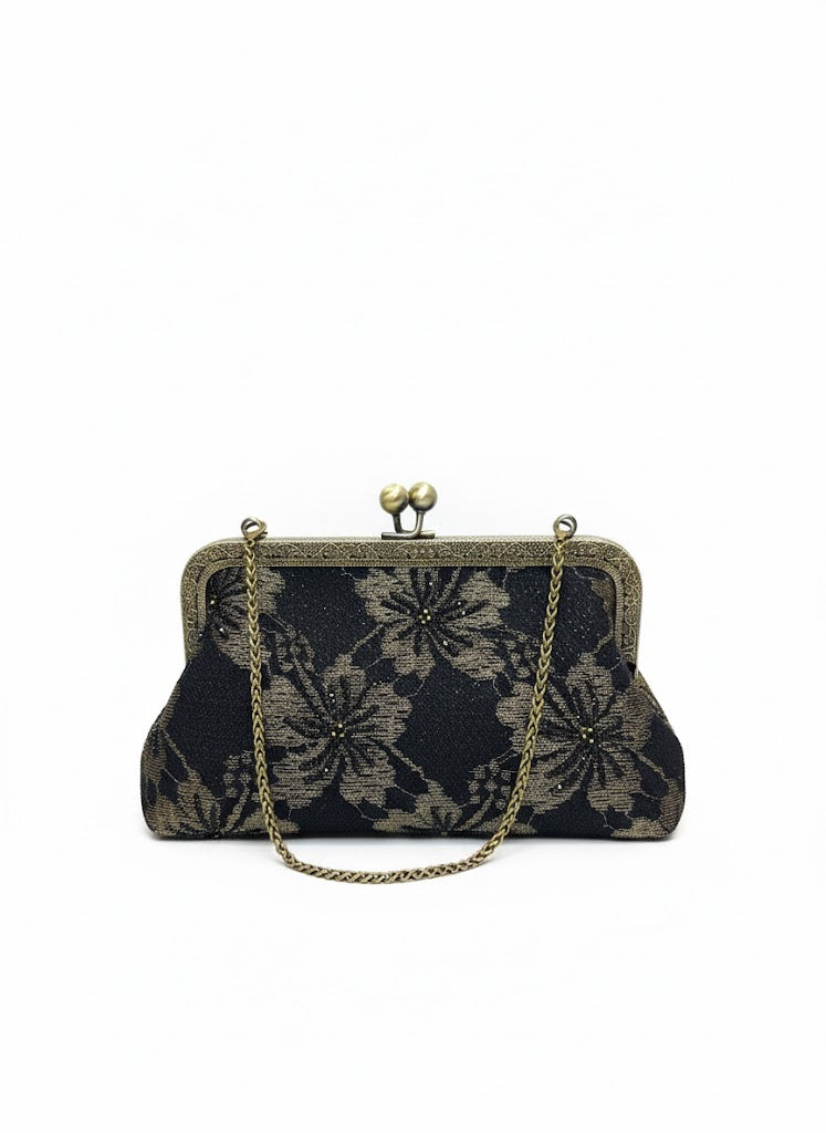 Vintage black clutch purse with bronze floral pattern and chain handle on white background