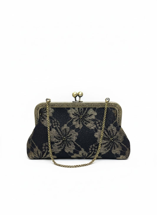 Vintage black clutch purse with bronze floral pattern and chain handle on white background